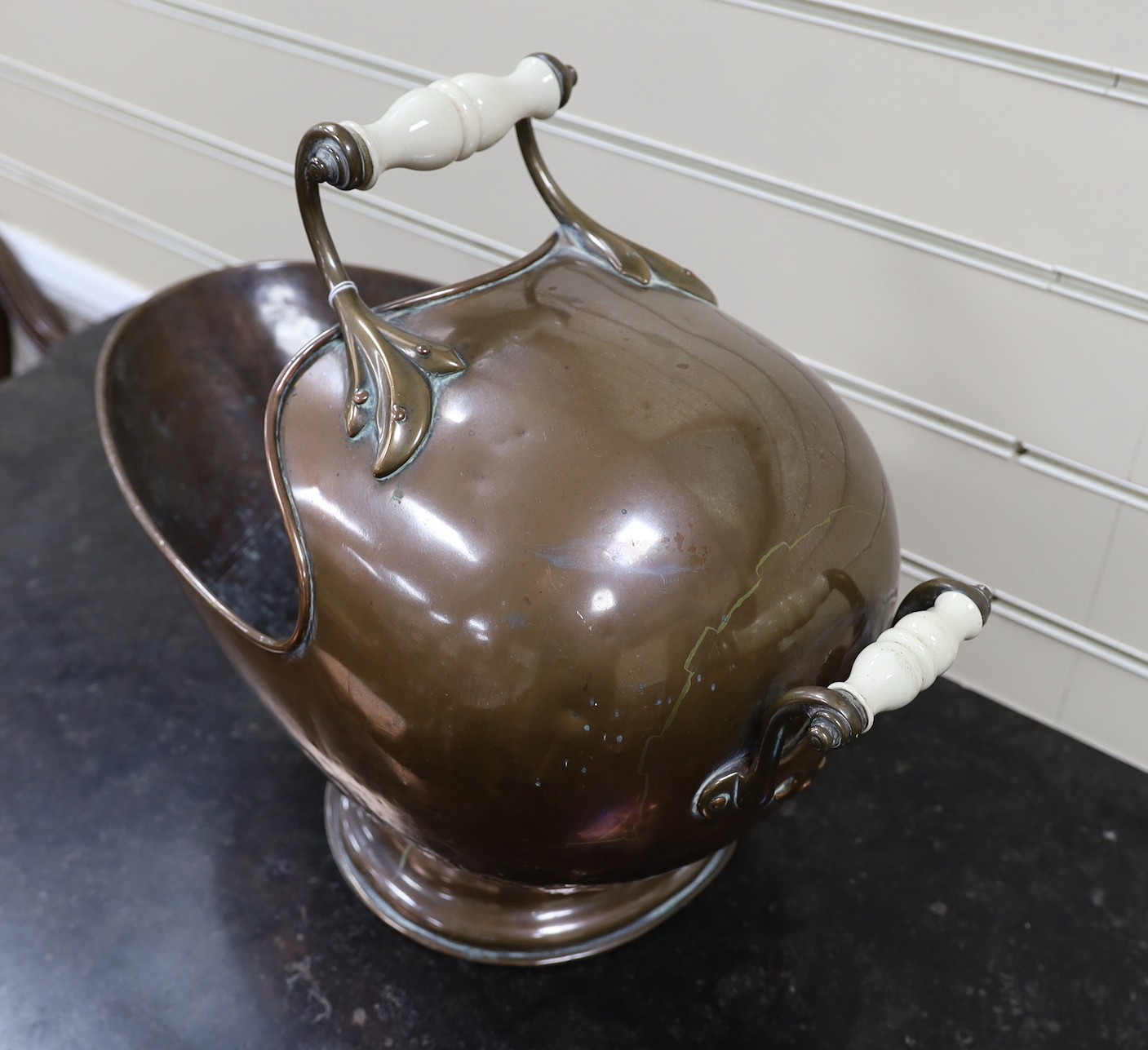 A helmet shaped copper coal scuttle, with ceramic handles, 52cms wide